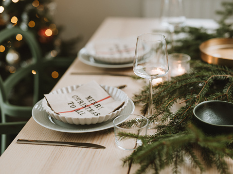 Christmas table place setting prepared for dinner party\nPlace setting on dining table with cutlery plate napkin and decorations for Christmas.