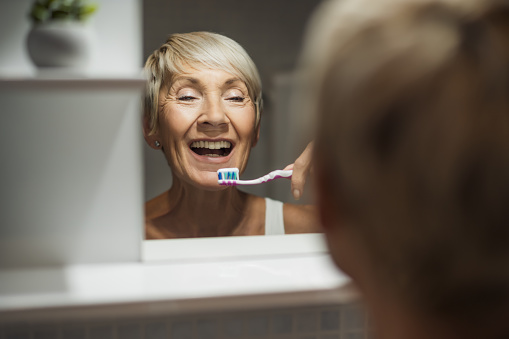 Mature woman is cleaning her teeth in bathroom.