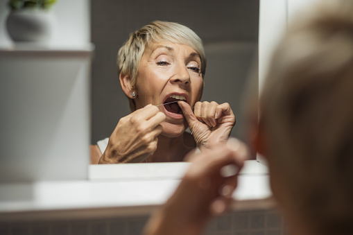 Mature woman is using dental floss to clean her teeth.