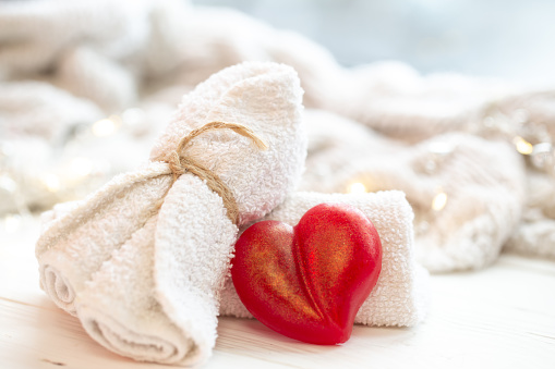 Spa composition with heart shaped soap towel closeup on blurred white background.