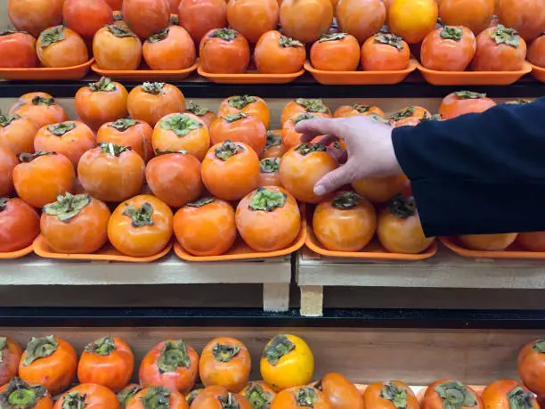 A female hand taking persimmon fruit in the supermarket