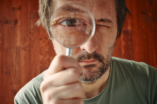 Curious man looking through magnifying glass with intense desire to know and understand