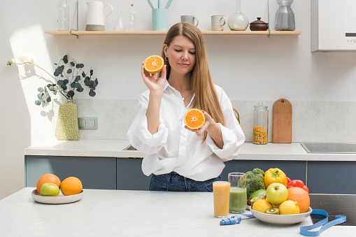 Joyful female on the kitchen playing with two half of orange, tasty juicy fruit instead eyes, healthy nutrition, fun and joy concept