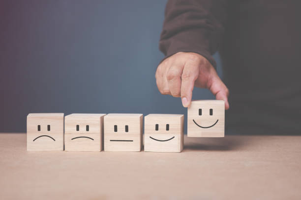 istock Customer Service Satisfaction and Assessment Survey Concept Customer's hand selects a smiley face symbol on a wooden block. 1443526105