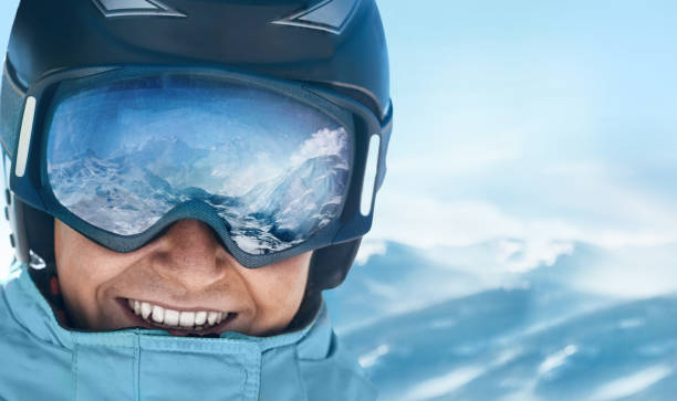 Close up of the ski goggles of a man with the reflection of snowed mountains.  A mountain range reflected in the ski mask.  Man  on the background blue sky. Wearing ski glasses. Winter Sports. stock photo