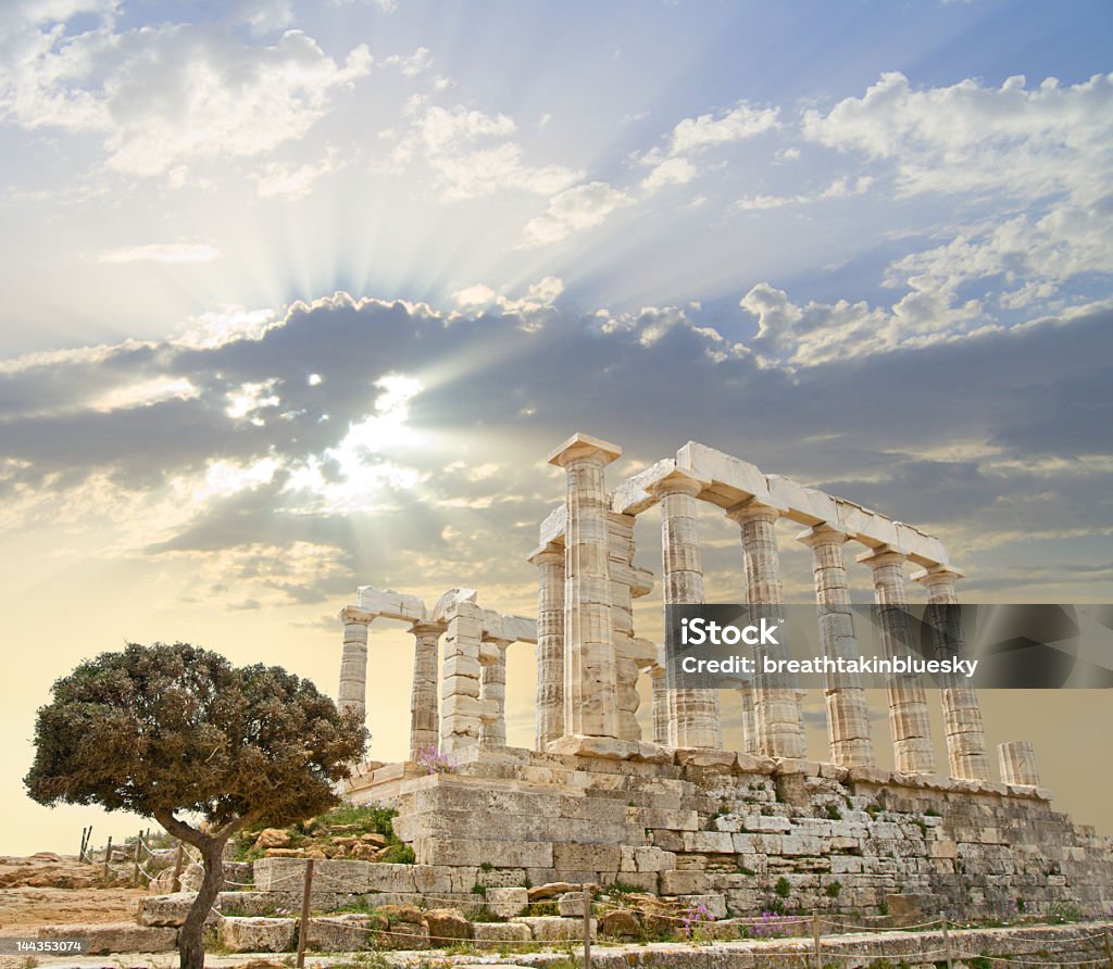 Poseidon's Temple in Greece with the sun behind the clouds Poseidon Temple is at the south tip of the Attica peninsula, near Athens. Poseidon is the greek name for Neptune, god of the sea.  Ancient Stock Photo