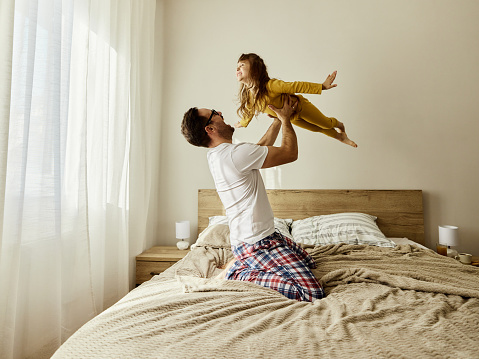Cheerful single father having fun with his small daughter during morning on a bed. Copy space.