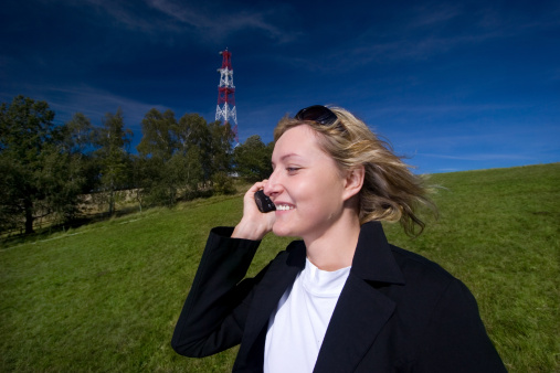 Young woman talking by using cell phone in green scenery near GSM antenne