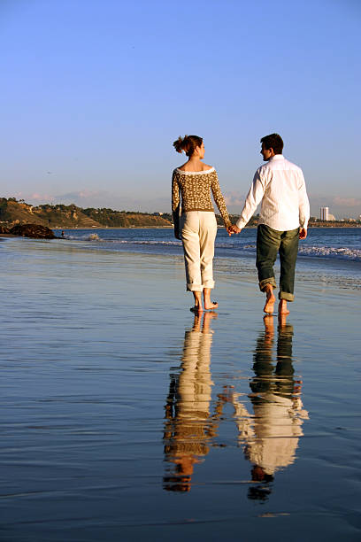 Couple walks down the beach holding hands stock photo