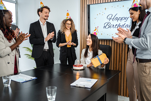 Group of people, men and woman celebrating birthday of their female colleague together in office.