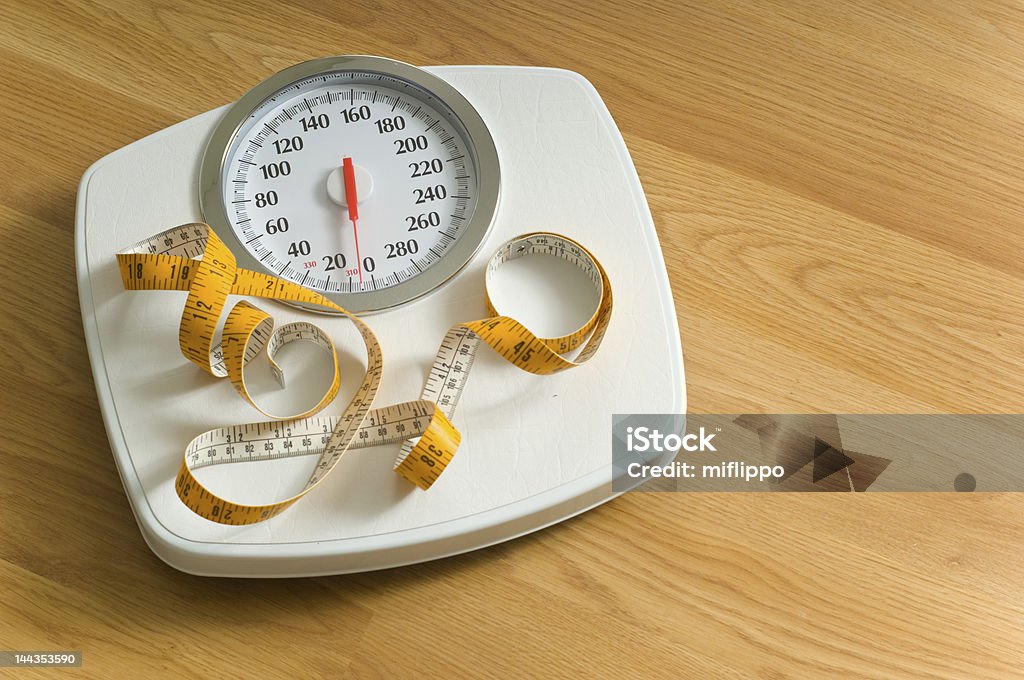 A white bathroom scale with yellow tape measure  Bathroom scales with yellow tape measure on top - dieting items Bathroom Scale Stock Photo