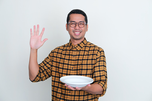 Adult Asian man smiling at camera while showing empty dinner plate