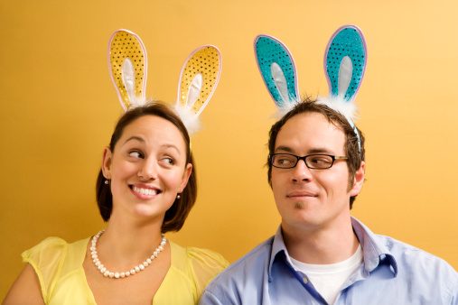 Caucasian mid adult couple wearing rabbit ears and looking at each other.