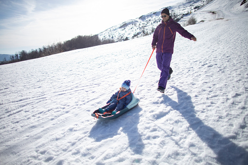 Father pulling one year old son on a baby sled, on a winter day.