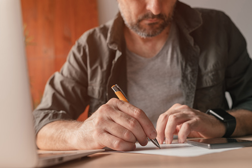 Freelancer writing notes on paper at home office desk, close up with selective focus