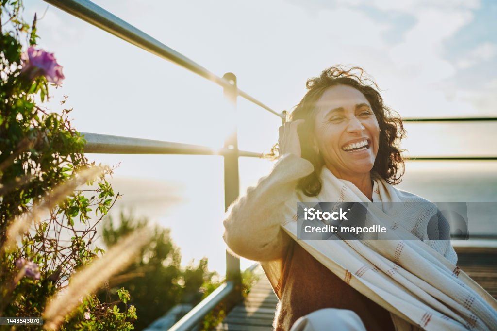 Laughing mature woman sitting by the ocean at sunset Mature woman wearing a pashmina laughing while sitting at a scenic viewpoint by the ocean at sunset Laughing Stock Photo