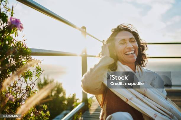 Laughing Mature Woman Sitting By The Ocean At Sunset Stock Photo - Download Image Now