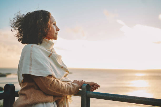 femme mûre regardant le coucher de soleil sur l’océan - introspection photos et images de collection