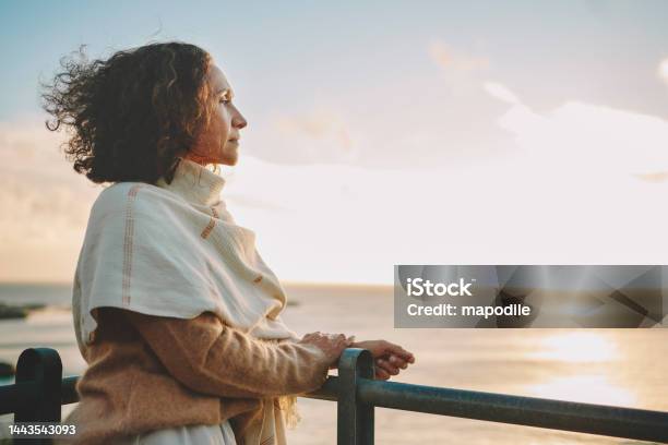 Mature Woman Watching The Sunset Over The Ocean Stock Photo - Download Image Now - Contemplation, Women, Mature Women
