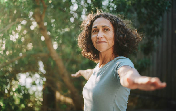 Smiling mature woman doing yoga outside in a park in summer Portrait of a smiling mature woman practicing yoga outside in a park in the summertime yoga stock pictures, royalty-free photos & images