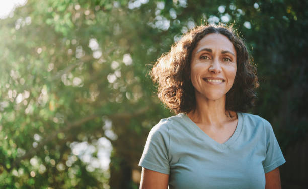 smiling mature woman standing in a park outdoors in the summertime - woman stockfoto's en -beelden