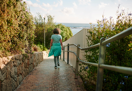 Rear view of a mature woman in sportswear walking down a scenic  brick footpath by the ocean