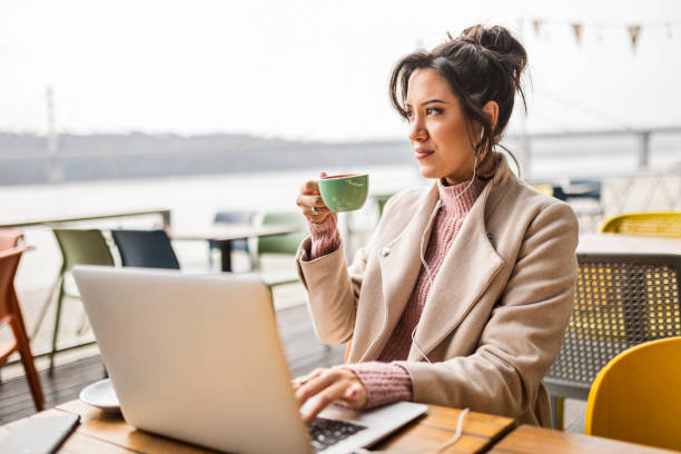 istock Young woman drinking coffee in cafe using laptop with headphones 1443545930