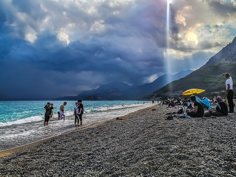 Antalya, Turkey - October 27, 2019: Turkish people relax on the Sarisu Beach against the backdrop of a mountain landscape, turquoise Mediterranean Sea and heavy storm clouds in Antalya