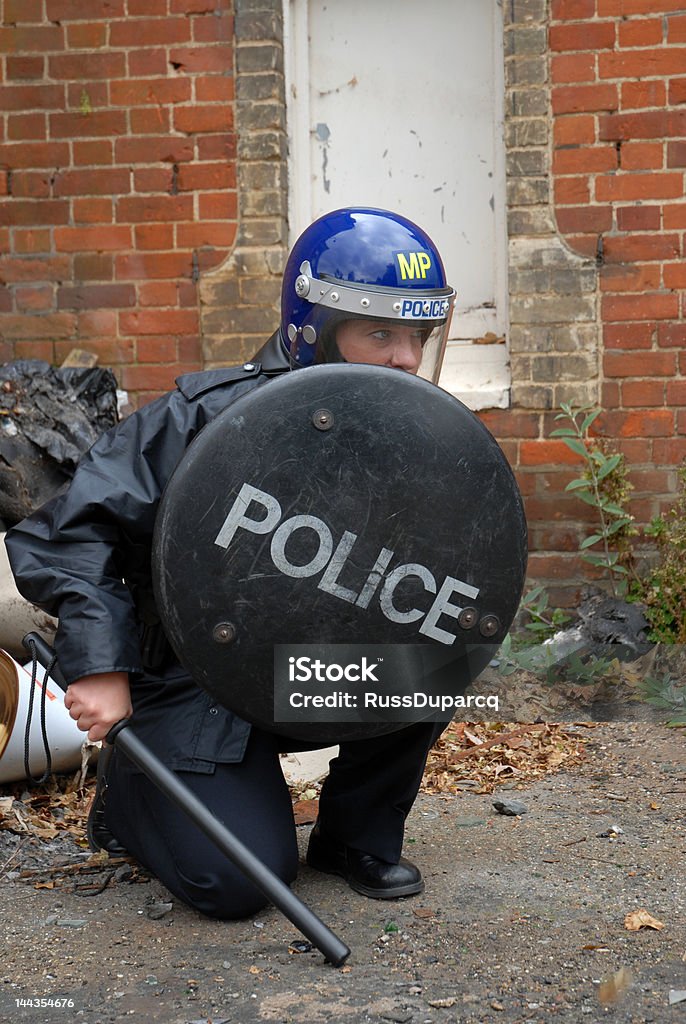 The Shield Female British police officer wearing riot equipment, kneeling. Police Force Stock Photo