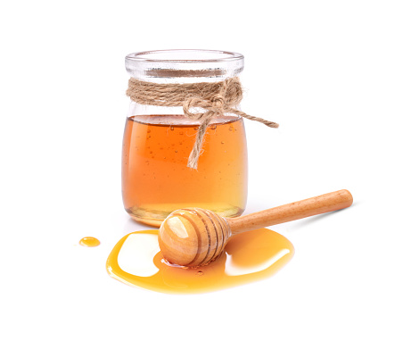 Honey in glass jar with honey dipper isolated on white background.