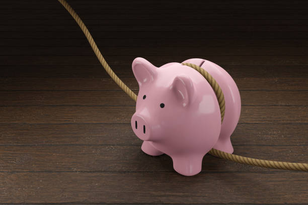rosa sparschwein wird durch ein seil auf einem holztisch festgezogen. veranschaulichung des konzepts der haushaltsstraffung und ausgabenkürzung - festziehen stock-fotos und bilder