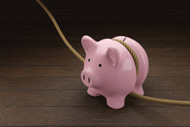 pink piggy bank is tightened by a rope on wooden table. illustration of the concept of budget tightening and reduction of spending - form fitted imagens e fotografias de stock