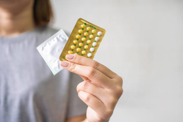 ontraceptif signifie : femme tenant la main des pilules contraceptives et du préservatif. protection, rapports sexuels protégés. contraception, concept de contrôle des naissances. - contraceptive sex education birth control pill condom photos et images de collection