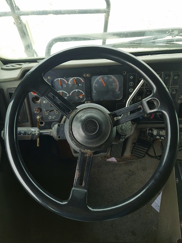 the steering wheel of an old coal mine truck, black with a dashboard background and dirty floor