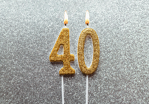 Gold number 40 celebration burning candle on silver glittering background