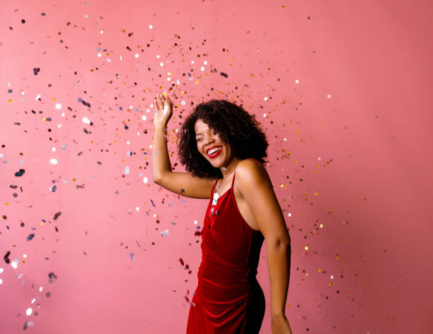 It's party time: A cheerful female in red dress smiling with her eyes closed while having fun. (studio shot, pink background)