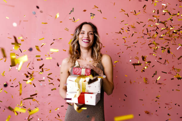 una mujer feliz de pie bajo la lluvia de confeti y sosteniendo bellamente - beautiful women gift christmas fotografías e imágenes de stock