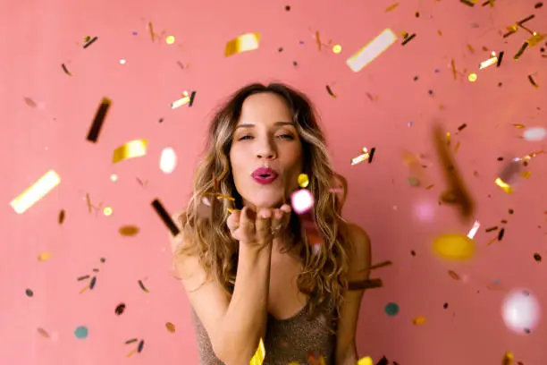 It's party time: A cheerful attractive Caucasian female in glitter brown dress sending kisses while looking at camera. (studio shot, pink background)