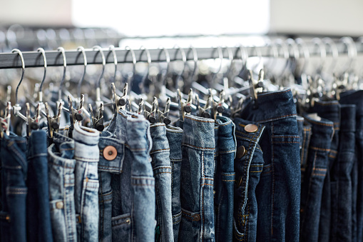 Close up of blue denim jeans in row on clothing rack at thrift shop, copy space