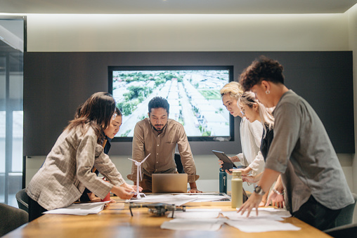 Business people is talking about new project in the meeting room. Team is standing around a table and listening their manager carefully.