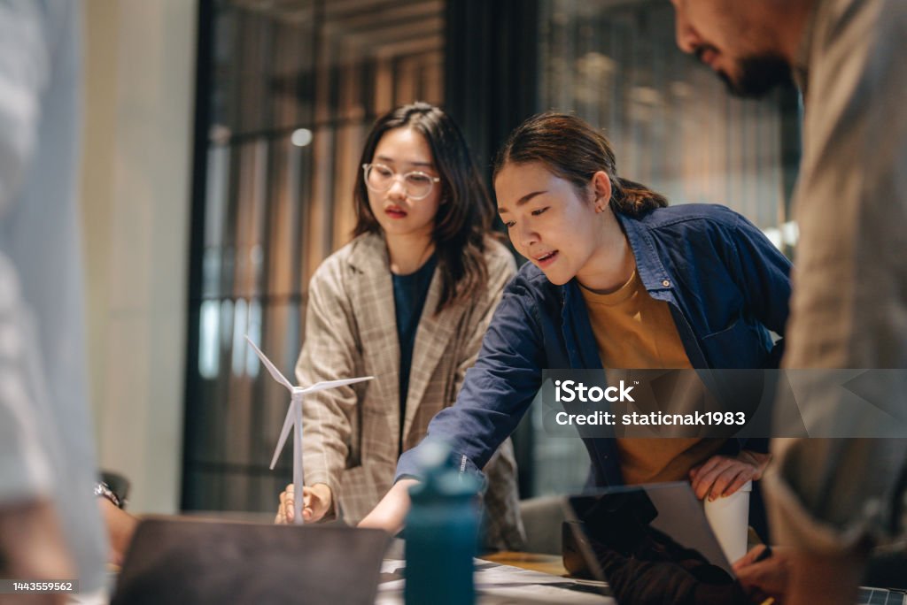 Asian architects team talking about a new project in the office. Business people is talking about new project in the meeting room. Team is standing around a table and listening their manager carefully. Asian and Indian Ethnicities Stock Photo