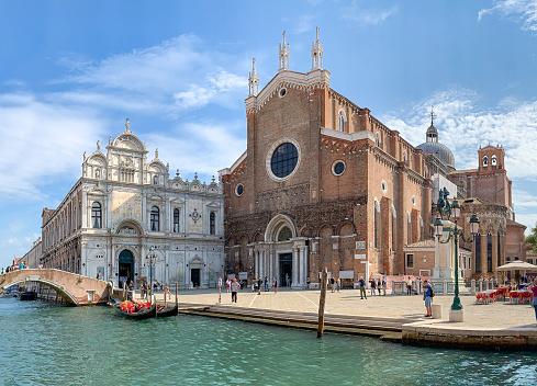 Large Venetian church of San Zanipolo with gondolas, bridge and town square on sunny day