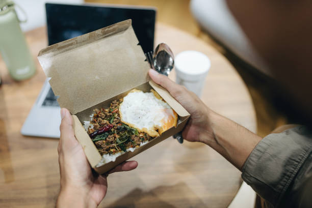 Asian female and male business partners eating  takeaway food and working at computer in office