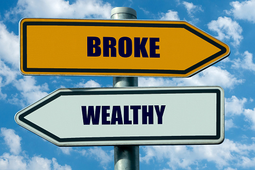two street signs pointing in opposite directions: broke - wealthy
