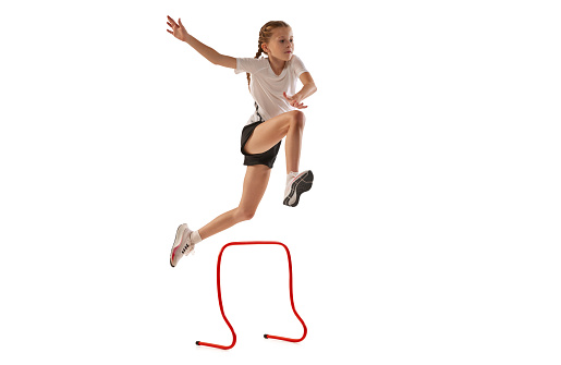 Jump. Dynamic portrait of little girl, professional athlete, runner, jogger at steeplechase training isolated over white background. Concept of sport, power, speed and competition