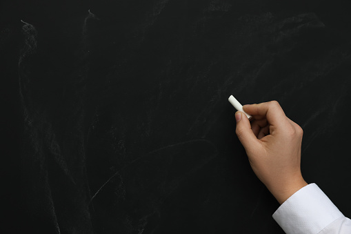 Man with white chalk near blackboard, closeup. Space for text