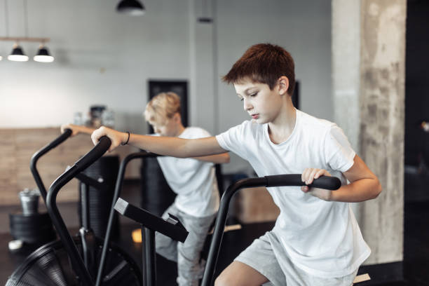 Two teenager boys are doing exercise with airbike in the gym. Cardio, strength training, fitness concept stock photo
