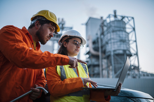 Two engineers using laptop at oil refinery on a night shift.