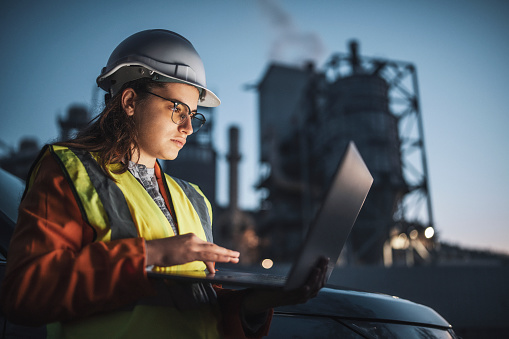 Female engineer doing working with laptop late at an oil and gas plant.