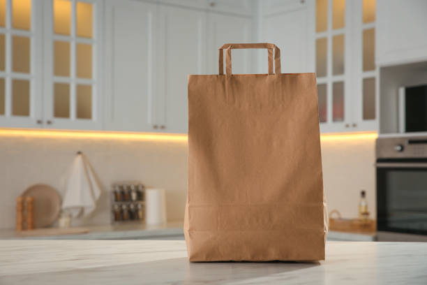 istock Paper shopping bag on white marble table in kitchen. Space for text 1443577575